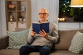 Happy bald senior man on sofa reading book at home