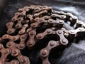 Old, aged, broken, and weathered motorbike chain on black fabric background