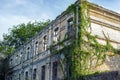 Old aged ruined abandoned two-storied brick building facade with brocken glass windows overgrown by green ivy. mystical
