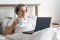 Old aging senior woman female in bed flat working home office holding laptop Jobs for Retirees cup