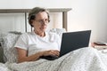 Old aging senior woman female in bed flat working home office holding laptop Jobs for Retirees