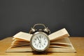 An old alarm clock with arrows stands in front of an open old book on a dark background. Royalty Free Stock Photo