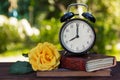 An old alarm clock, a stack of books and a rose on a wooden table. Books, a watch and a rose on a green natural background. Copy s Royalty Free Stock Photo