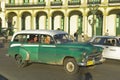 An old American green car and taxi driving through Old Havana, Cuba