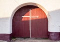 Old ancient entrance maroon gate door with a white cross on them against a solid white brick wall. Entrance to the Christian monas