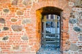 An old ancient metal door with a sturdy prison bars on a thick, wide wall of red clay scratched cracked brick Royalty Free Stock Photo