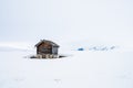 A old and ancient wooden cabin outdoors in beautiful snow covered mountains and foggy scenery with crosscoutry skiiers in the back