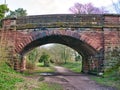 An old, arched, sandstone bridge over a disused railway line, now the Wirral Way, a public walking path in north-west England, UK