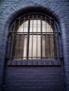 Old arched window in a black brick wall with heavy metal bars Royalty Free Stock Photo