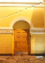 Old arched wooden door with four panels of brown painted wood in an old yellow building with arches and columns Royalty Free Stock Photo
