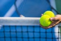 Old asian man hold two tennis balls in left hand, selective focus, blurred racket, net and green tennis court as background Royalty Free Stock Photo