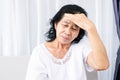 Old Asian woman suffering from headache, migraine and feeling dizzy sitting at sofa hand holding her head Royalty Free Stock Photo