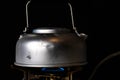 Old banged up steel kettle boiling water on a camping gas stove with a blue flame. Isolated on black background. Royalty Free Stock Photo