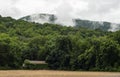 An old barn sits under green mountains and fog.