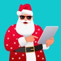 An old bearded Santa Claus in sunglasses and a red suit with white snowflakes is standing with a tablet in his hand. Santa is a
