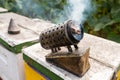 Old Beekeeper Smoker smokes white smoke. Apiary background. Grungy open smoker stands on the hive