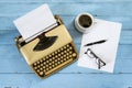 Old beige typewriter from the 1950s with paper, coffee and glasses on a blue painted wooden table, high angle view from above Royalty Free Stock Photo