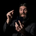 Old believer senior priest with a smartphone, bearded old man is calling on a dark background