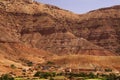 Old berber village oasis with houses build of clay bricks in front of impressive high rugged red mountain face, Gorges du Dades,