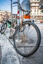 Vintage rusty bicycle with metal lamp on helm parked at bike rack on the sidewalk