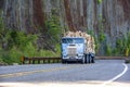 Old big rig cab-over semi truck transporting paper recycling on flat bed semi trailer driving on mountain winding road with rock