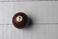 Old billiard ball number 7 brown color on white wooden table background, copy space Royalty Free Stock Photo