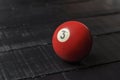 Old billiard ball number 3 red color on black wooden table background, copy space