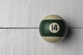 Old billiard ball number 14 striped white and green on white wooden table background, copy space Royalty Free Stock Photo