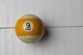 Old billiard ball number 9 striped white and yellow on white wooden table background, copy space Royalty Free Stock Photo