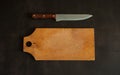 An old birch cutting board and a chef`s knife on a dark concrete background. Royalty Free Stock Photo