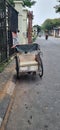 An old black and cream rickshaw that is empty and has no passengers stopping on the side of the road.