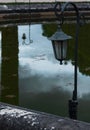 Old black iron street lantern in the park against the background of reflections in the water Royalty Free Stock Photo