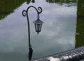 Old black iron street lantern in the park against the background of reflections in the water Royalty Free Stock Photo