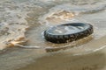 Old black rubber tire left on beach, environment pollution concept, selective focus, color toned picture. Discarded old tyre in bl Royalty Free Stock Photo