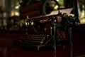 An old black rustic typewriter is on a desk in a 19th century office and ready to be worked on