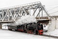 Old black steam locomotive in Russia in the winter on a background of bridge Royalty Free Stock Photo