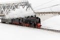 Old black steam locomotive in Russia in the winter on a background of bridge Royalty Free Stock Photo