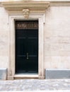 Old black wooden door set in an ornate white stone carved classical style frame and wall with pale sloping tiled pavemtn in the st Royalty Free Stock Photo