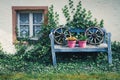 Old blue decoration bench with two wooden wagon wheels and two pink flower pots Royalty Free Stock Photo