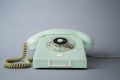 Old blue rotary telephone with twisted cord on gray background. Retro landline phone with rotary dialer and handset