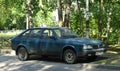 An old blue rusty car is parked in the courtyard of a residential building