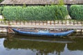 An old blue wooden boat, moored to the shore, with a hedge and thatched roof in the background. Royalty Free Stock Photo