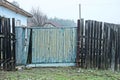 Old blue wooden gate with broken planks and part of a black fence Royalty Free Stock Photo