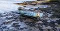 Old blue wooden rowing boat on the beach with seaweed on the sand low tide with slip way Royalty Free Stock Photo