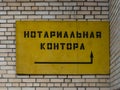 Old yellow board of the closed notarial office in Russia with arrow indicating the entrance. Brick wall in background.