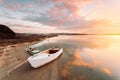 Old boat moored on sandy shore with sunrise reflections