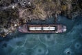 Old boat ship, trapped, frozen in winter ice lake, docked in pier, aerial top down view