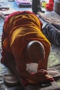 An old bold monk wearing traditional red and yellow cloathes praying in prostration in front of Jokhang temple in Lhasa