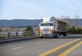 Old bonnet cab-over big rig semi truck with bulk trailer running on the road with protection fence on the side Royalty Free Stock Photo