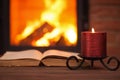 Old book and candle in front of fireplace
